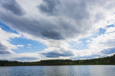 Ormanlık bir kıyı ile küçük bir göl üzerinde güzel bulutlu gökyüzü. 