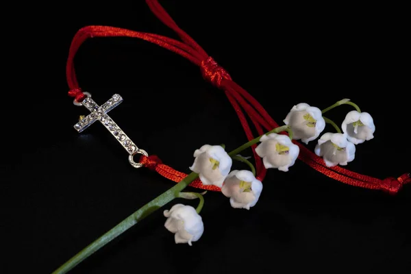 Red lace charm bracelet and white lily of the valley flower.