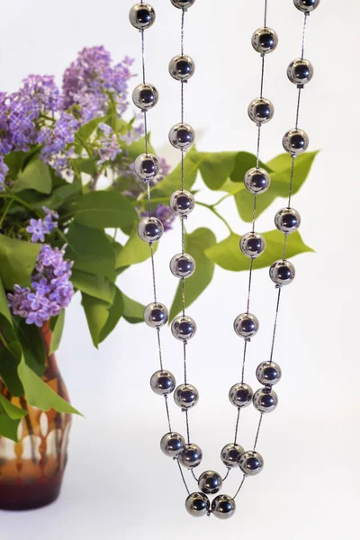 Zwei Fäden aus runden, glänzenden Perlen und ein Strauß Flieder. — Stockfoto