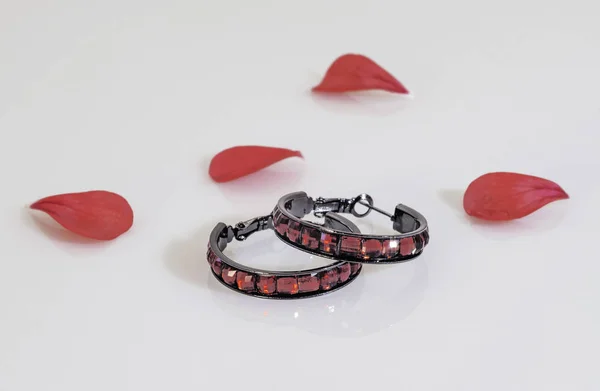 Dois brincos redondos escuros com pedras vermelhas brilhantes e pe flor vermelha — Fotografia de Stock