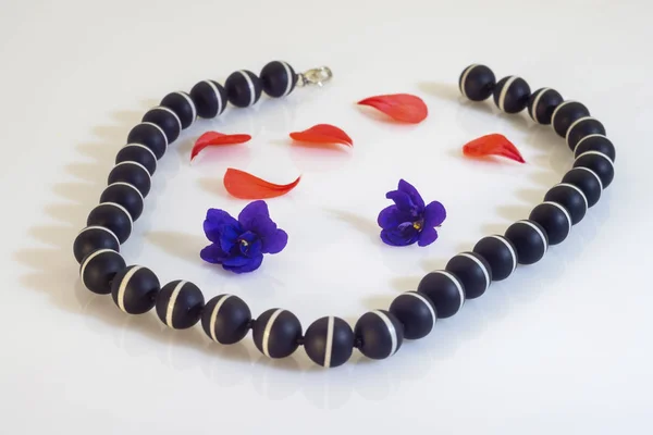 Schwarze kugelförmige Perlen mit weißem Streifen, lila Blüten und — Stockfoto