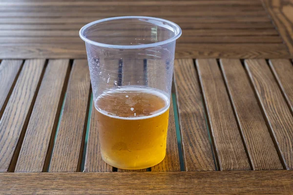 Beer with white foam in a plastic transparent cup on a wooden ta — Stock Photo, Image