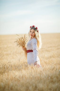 Buğday tarlasında beyaz bir elbise giymiş uzun sarı saçlı genç beyaz bir kadın.