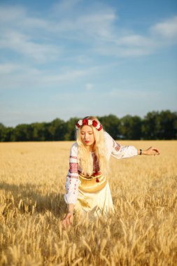 Buğday tarlasında beyaz bir elbise giymiş uzun sarı saçlı genç beyaz bir kadın.