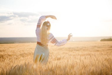 Buğday tarlasında beyaz bir elbise giymiş uzun sarı saçlı genç beyaz bir kadın.