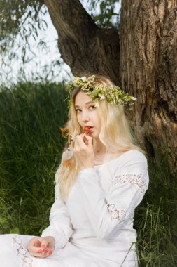 Beyaz elbiseli, uzun sarı saçlı genç beyaz kadın çilek yiyor.