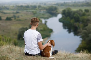 Genç çocuk köpeğiyle nehrin üzerinde oturur.