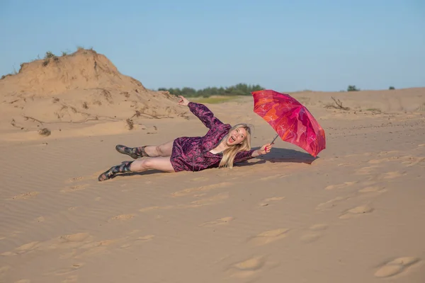 一个金发碧眼的年轻女人 穿着雨衣 在沙漠中带着雨伞 — 图库照片