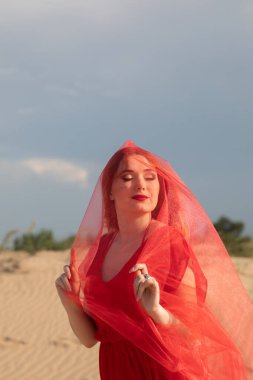 Kırmızı elbiseli güzel bir kadın çölde dans ediyor.