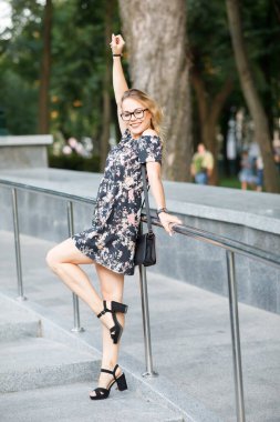 Sarışın, kıvırcık saçlı, parkta gözlük takan güzel bir genç kadın.