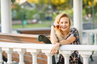  Sarışın, kıvırcık saçlı, elbise giyen ve gözlüklü güzel bir kadın akşam vakti parkta oturuyor.