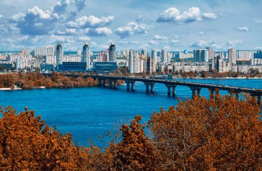 Nehir kıyısındaki gökdelenler. Büyük nehrin üzerindeki köprü. Yüksek binalar. Şehirde bir iş günü. Yeşil yaz ağaçları.