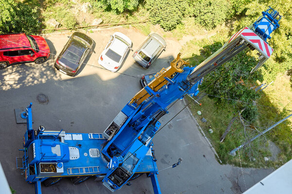 2025-03-09, Kyiv, Ukraine. Mobile crane with extended boom working near parked cars in a residential area. Heavy construction equipment used for lifting and building operations in urban environment.