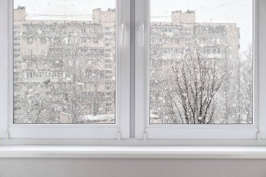 Yoğun bir kar yağışı ve konut binasının plastik çift camlı penceresinden bakın. Kış mevsimi, kar fırtınası, şehir manzarası, soğuk hava.