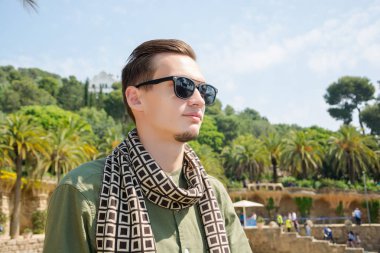 Güneş gözlüğü ve bir eşarp, palmiye ağaçları Guell Park, bir arka plan üzerinde bir turist olan genç bir adam mimar Gaudi Barcelona, İspanya