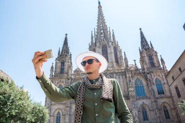 Genç bir adam, bir turist gözlük ve şapka, The Cathedral Holy Cross ve Aziz Eulalia Barcelona, İspanya'nın önünde selfie yapar