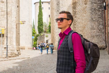 Ayakta ve merkezi Girona yakınındaki Saint Felix Bazilikası'na (Esglesia de Sant Feliu), gülümseyen bir sırt çantası ile genç bir turist İspanya