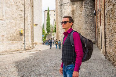 Ayakta ve merkezi Girona yakınındaki Saint Felix Bazilikası'na (Esglesia de Sant Feliu), gülümseyen bir sırt çantası ile genç bir turist İspanya