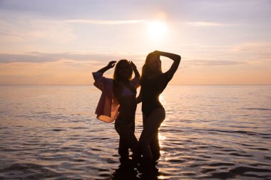 İki güzel kız öğrenciler pembe günbatımı deniz arka plan, siluetleri plajda dans ediyor