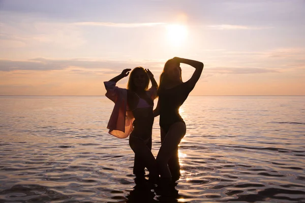 İki güzel kız öğrenciler pembe günbatımı deniz arka plan, siluetleri plajda dans ediyor