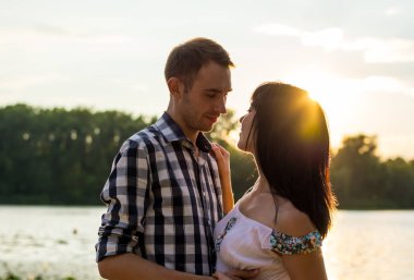 Adam genç kadın öpecek ve onu vasıl günbatımı geçmiş sarılarak. Sevgi dolu bir çift - karı koca, günbatımı Nehri yakınında ışınları