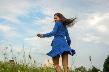 Güzel gülümseyen genç kadın dans ve bir çayırda çiçekler arka plan, bir çiçekli mavi elbiseli yaz fırtınası.