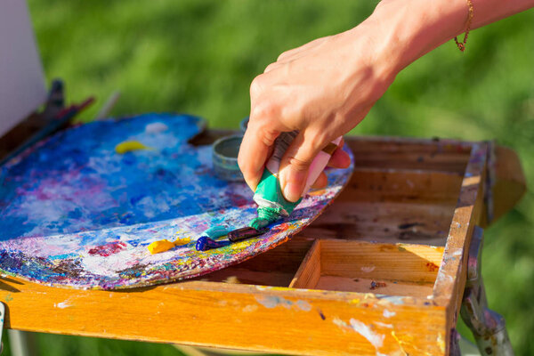 The artist's hand, which squeezes the oil paint from the tube into the palette on the easel, outdoor