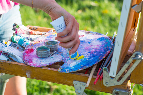 The artist's hand, which squeezes the oil paint from the tube into the palette on the easel, outdoor
