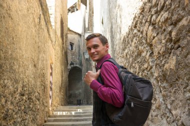 Genç yakışıklı turist adam gülümseyerek, antik sokaklarda Girona, İspanya bir sırt çantası ile