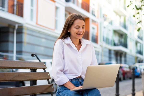 年轻美丽的笑女性与笔记本电脑坐在长椅上的商业部分城市 年轻美丽的女人 自由职业者 在笔记本电脑上夏天工作 — 图库照片