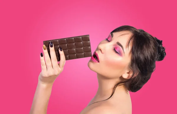 女性は チョコレート 美しい若い女性は ピンクの背景のチョコレートを食べています チョコレートを食べる少女 コンセプト — ストック写真