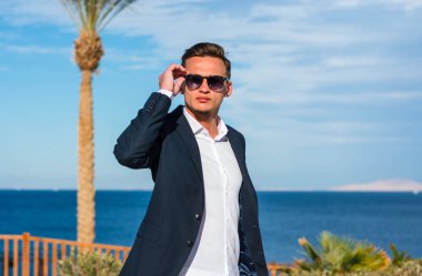 Deniz arka plan ve palmiye ağaçları, elbiseli genç yakışıklı adam. Moda Model