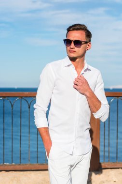 Yakışıklı delikanlı adam beyaz bir gömlek ve bir plajda denize arka plan, beyaz pantolon. Moda Model