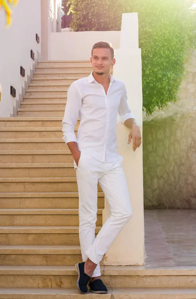 Ung kille i en vit skjorta står och ler nära trapporna och — Stockfoto