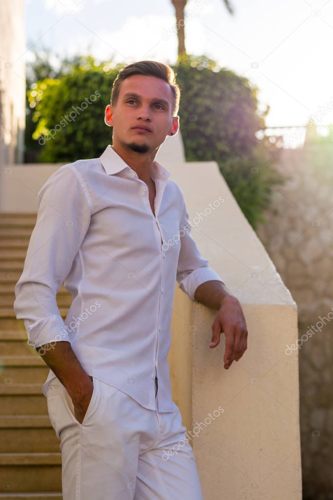 Young guy in a white shirt and sunglasses stands near the stairs