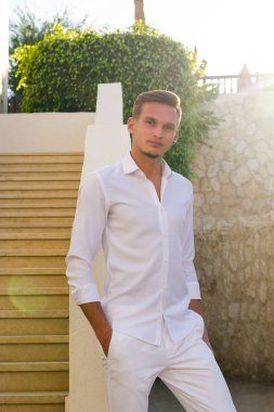 Beyaz gömlekli bir genç adam standları ve gülümsüyor merdivenlerden ve