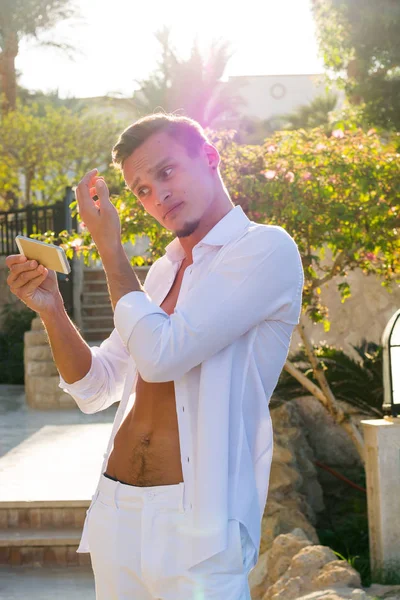 Young handsome guy in a white shirt straightens his hair, lookin — Stock Photo, Image