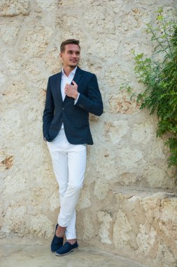 Genç yakışıklı adam ayakta yakınındaki bir takım elbise ve beyaz pantolon içinde bir 