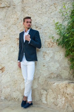 Genç yakışıklı adam ayakta yakınındaki bir takım elbise ve beyaz pantolon içinde bir 