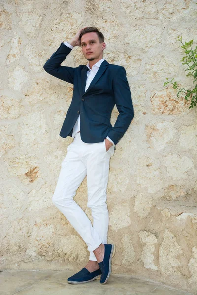 Young handsome man in a suit and white pants at standing near a — Stock Photo, Image