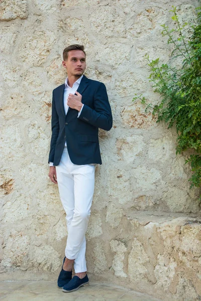 Genç yakışıklı adam ayakta yakınındaki bir takım elbise ve beyaz pantolon içinde bir 