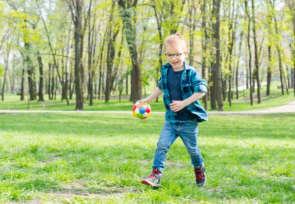Маленький мальчик, хипстер в очках с мячом бежит через пар — стоковое фото