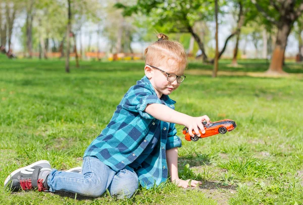 Мальчик в очках играет с игрушечной машиной в парке в спрее — стоковое фото