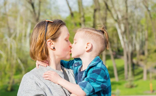 Mom kisses her boy in the park in spring.