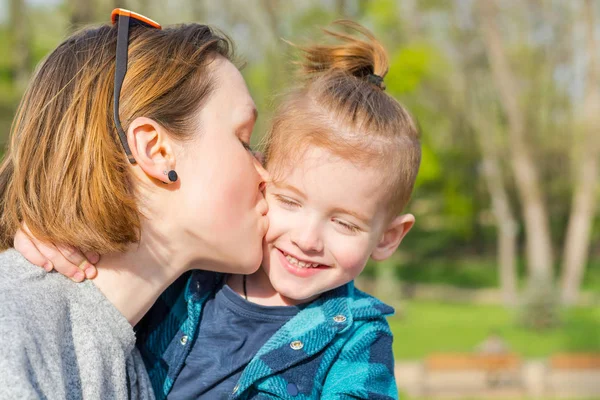 Мама целует своего мальчика, который смеется в парке — стоковое фото