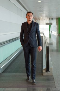 Takım elbiseli genç ve yakışıklı bir adam havada yürüyen merdivenden indi.