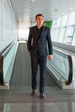 Takım elbiseli genç ve yakışıklı bir adam havada yürüyen merdivenden indi.