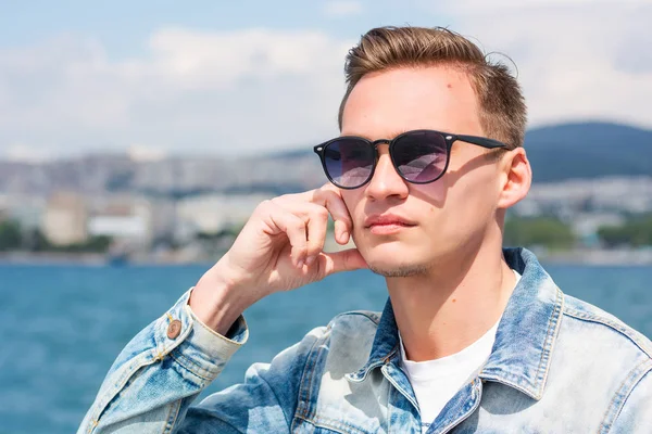 Um homem bonito jovem em óculos de sol no fundo da paisagem marinha — Fotografia de Stock