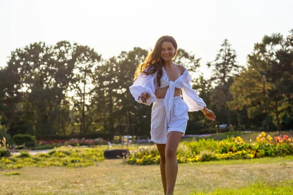 Krásná usměvavá mladá žena běhá v bílých šatech na louce — Stock fotografie