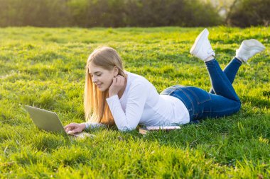 Genç güzel kadın öğrenci bir dizüstü bilgisayar ile çim üzerinde yalan